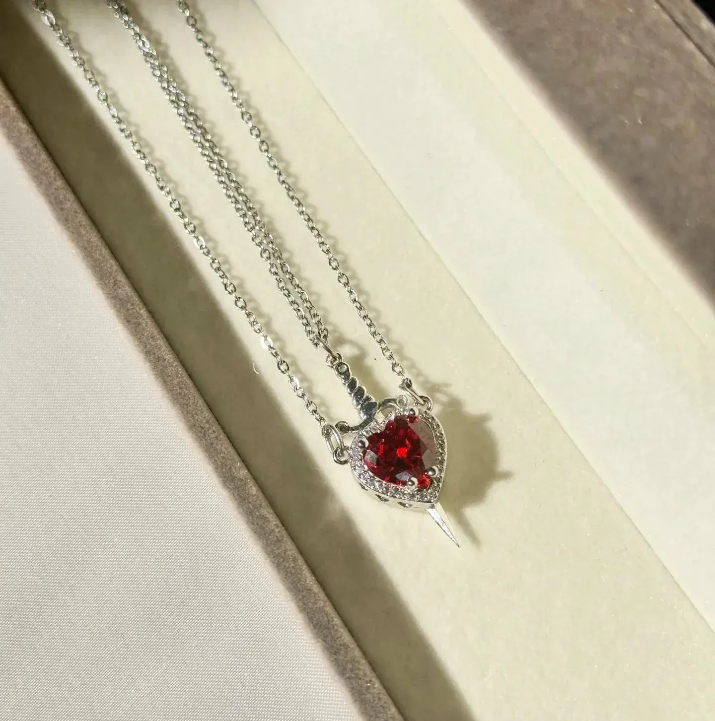 Necklace with a heart-shaped red gemstone pendant on a beige background